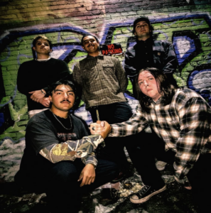 5 member band pose in front of graffiti wall